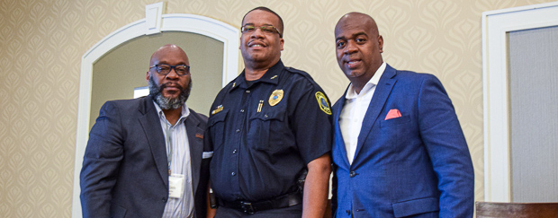 Three men stand together smiling.