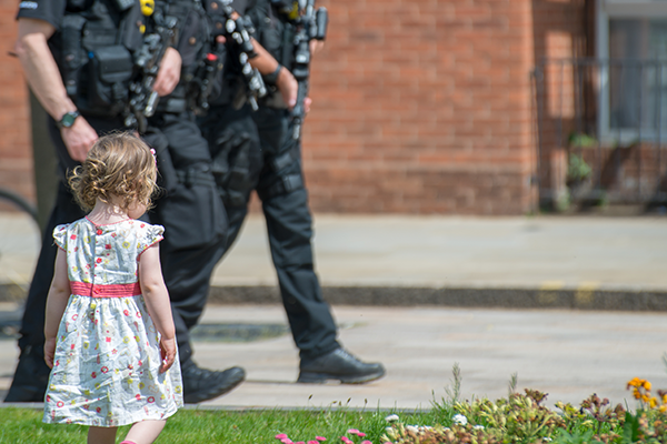 A child crossing the street with police officers in the background.