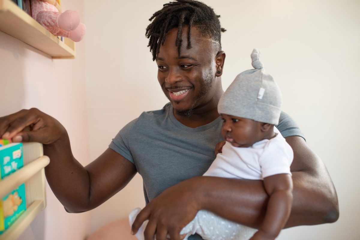 Smiling man holds his baby and looks at box of diapers