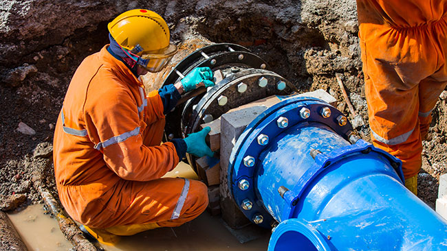 Person in work jumpsuit fixing large water pipe
