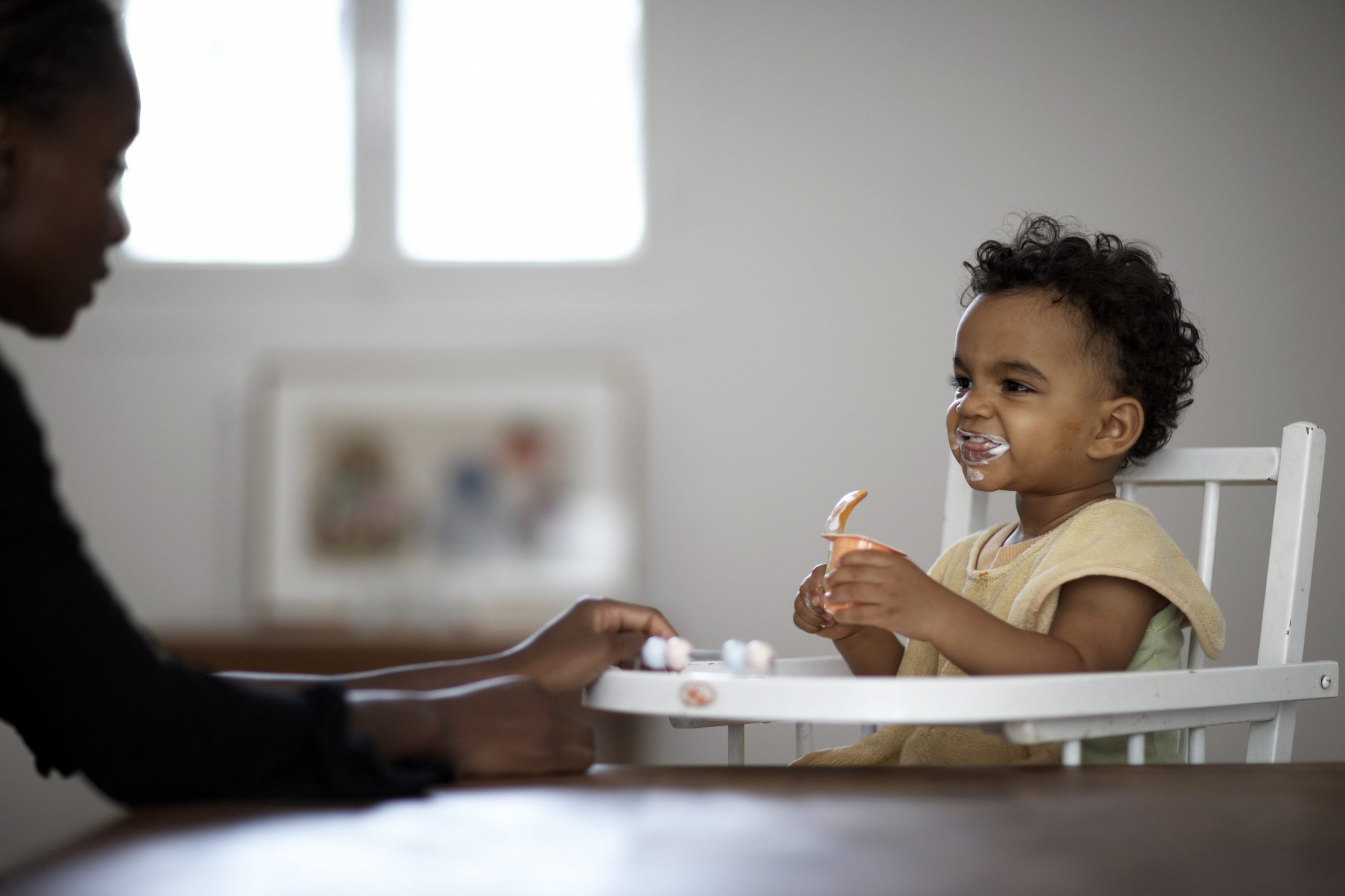 A parent feeds a young child in a high chair.