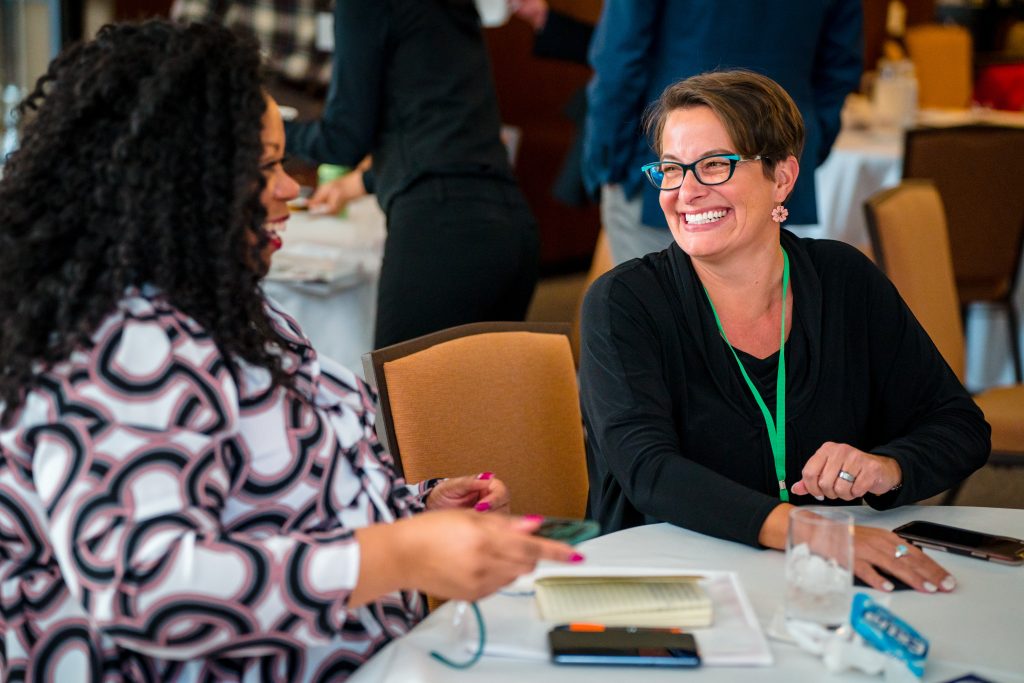 Two women mayors chatting at a table in a meeting room.