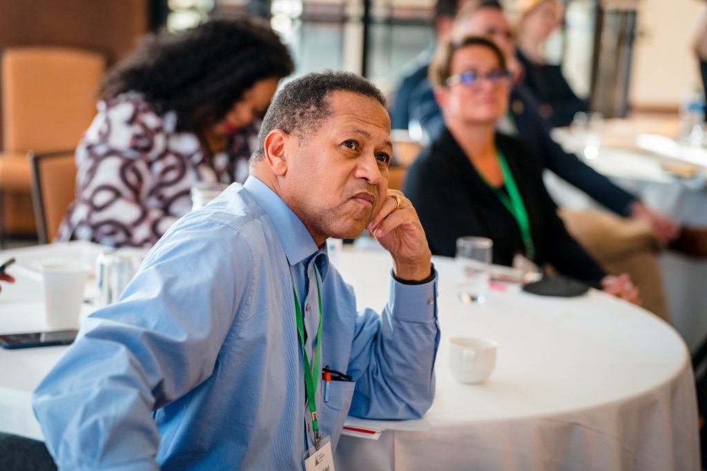 A mayor sits at a table listening to a presentation.