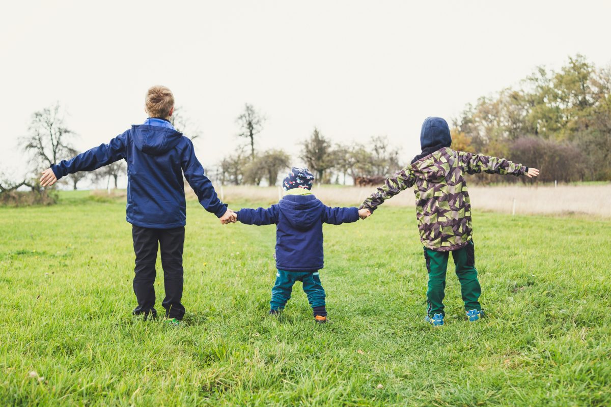 Three children holding hands outside.