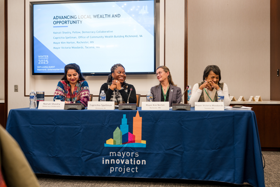 A group of panelists sit at a speakers table.