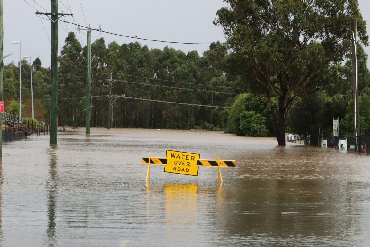 Flooded street with a yellow sign reading "Water Over Road"