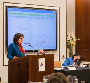 Mayor Katjana Ballantyne speaks at a podium with a large graph behind her.