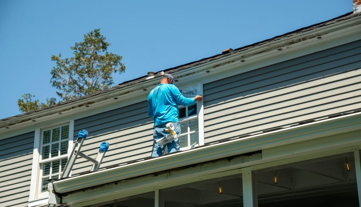 Man on the roof of a home making repairs to a window.